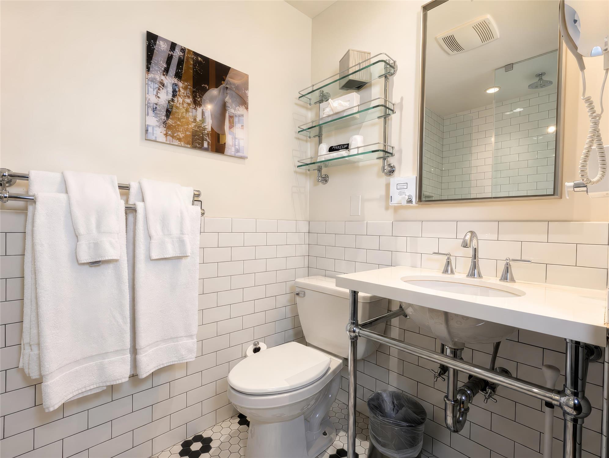 A clean and modern bathroom with white tiles, a toilet, sink, and shower.
